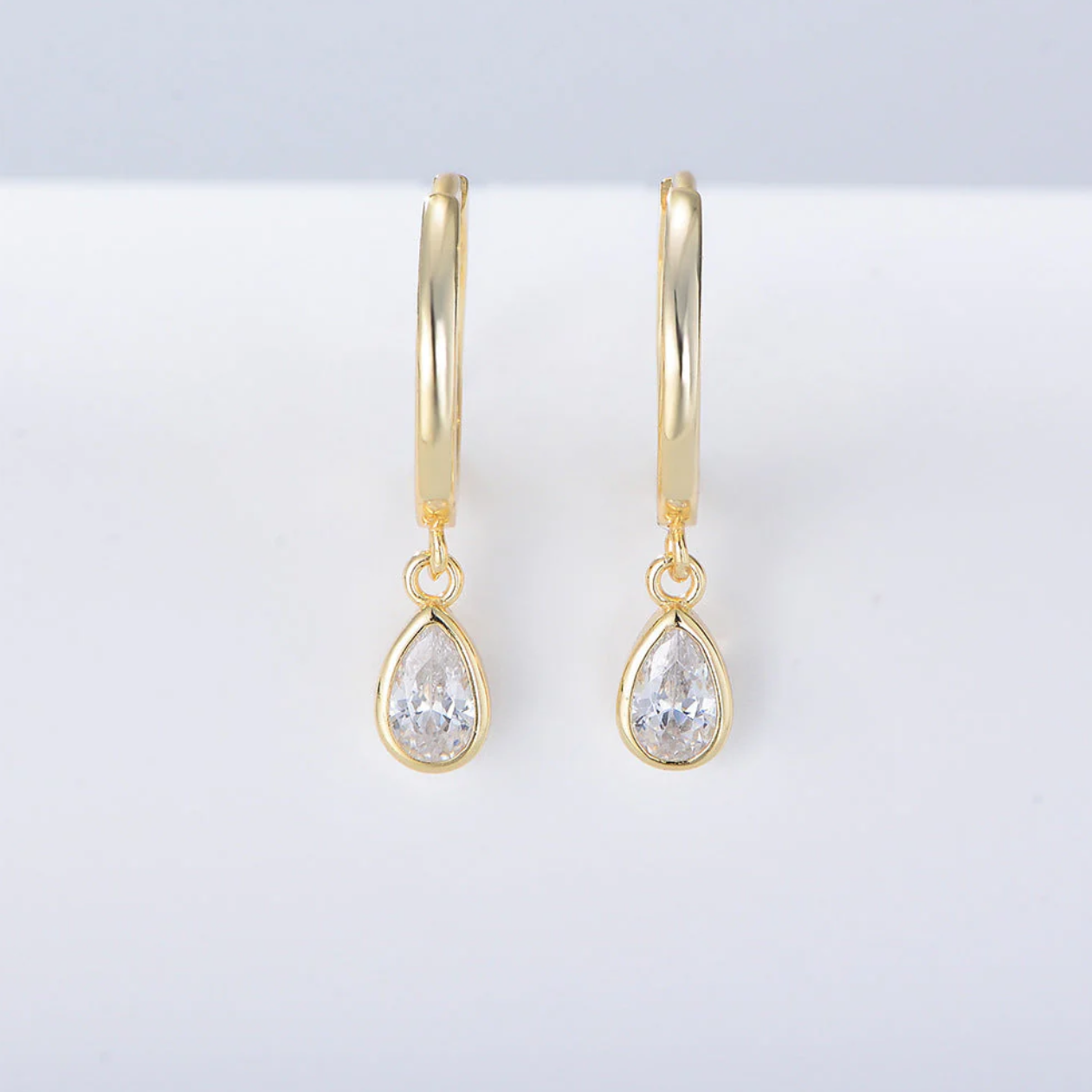 Each earring features a pear-shaped diamond simulant, beautifully bezel set for a sleek, contemporary finish that enhances sparkle while keeping the design timeless and secure. The soft drop silhouette flatters the face and adds a subtle glow, making these earrings perfect for both day wear and evening elegance.